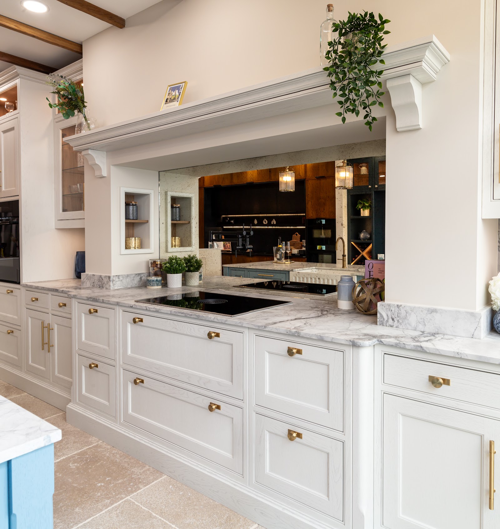 An in-frame display in the Chichester showroom — pale painted cabinetry with aged-brass cup handles and knobs, marble worktops and an induction hob.